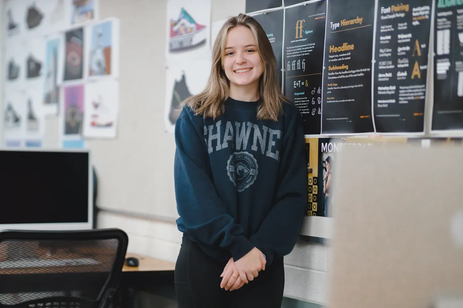 Student standing beside wall with posters made by design students