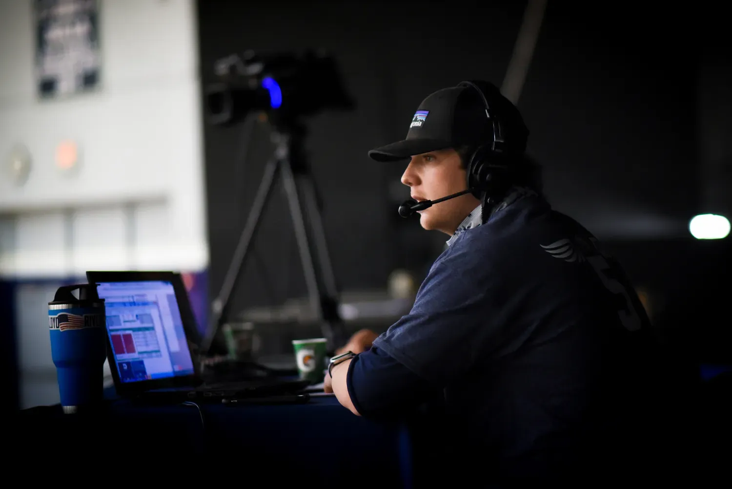 Student with headset and computer watching a live basketball game