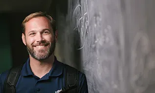 Teacher leaning against blackboard smiling