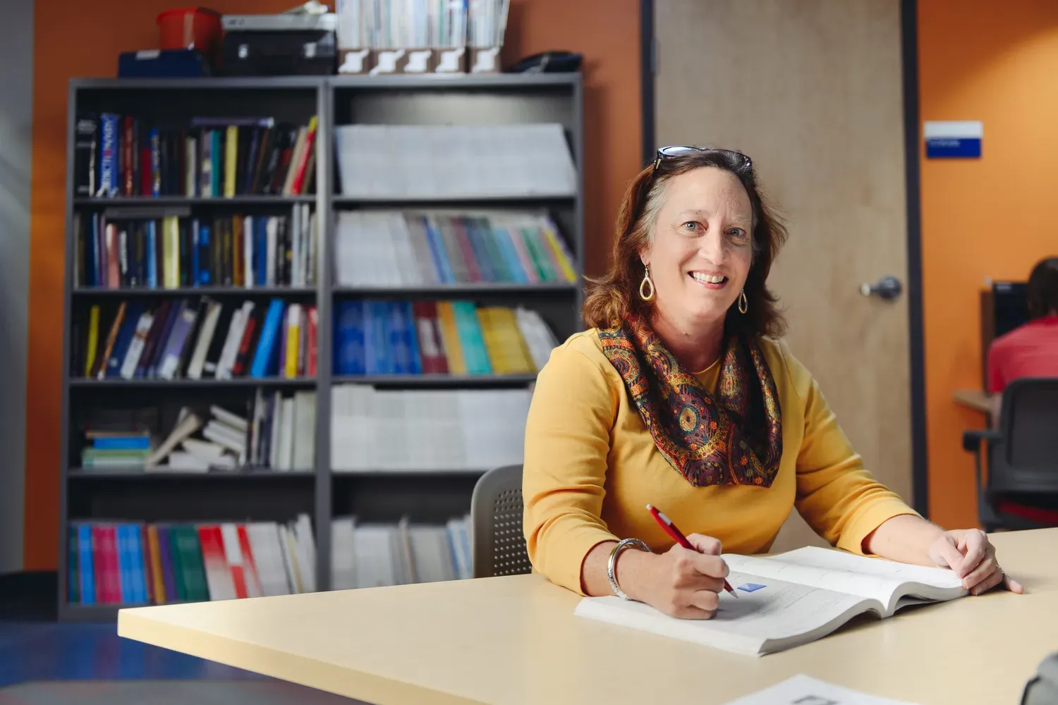 Teacher sitting at desk smiling while holding papers
