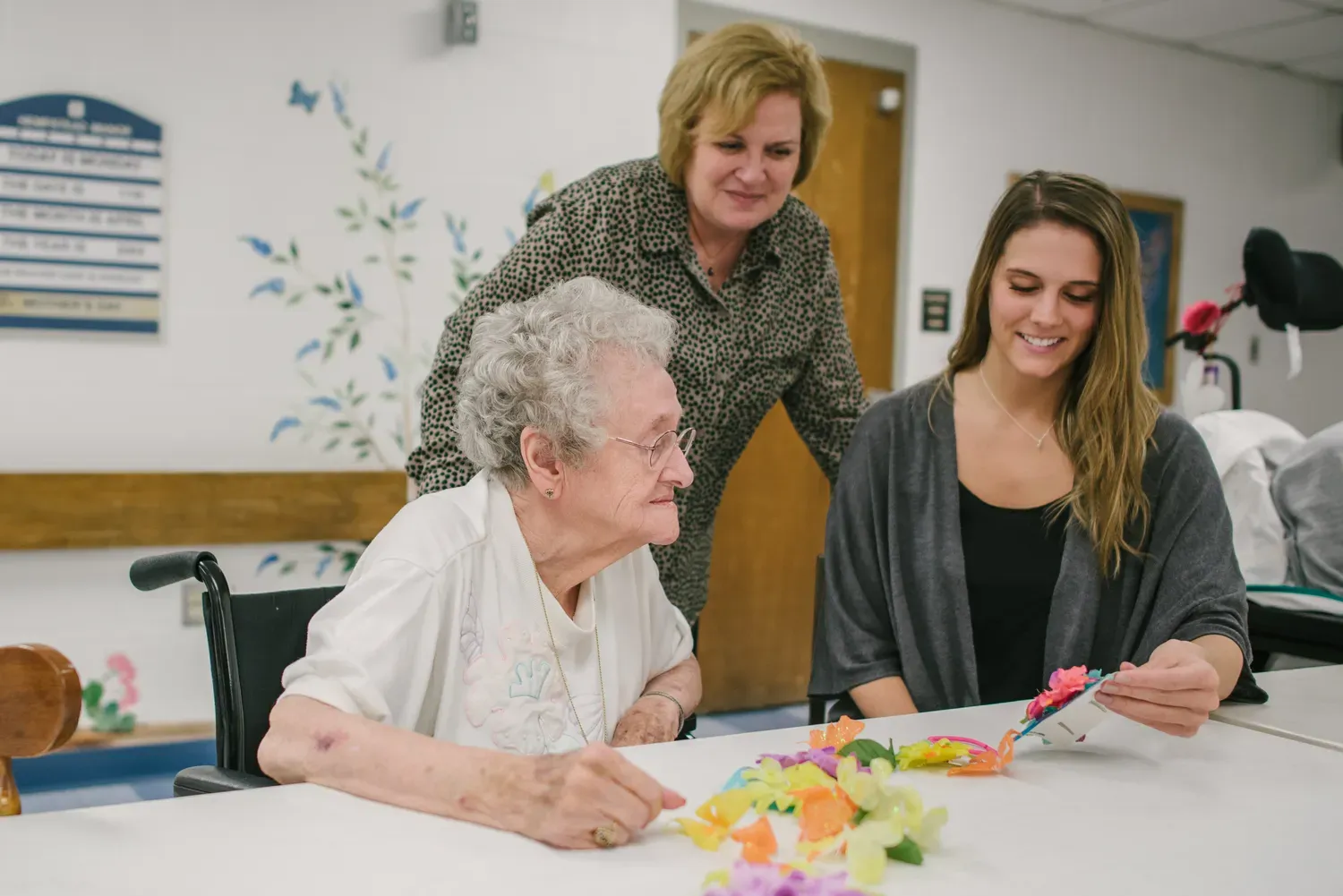 Student sitting at table with elderly woman assisting with a craft